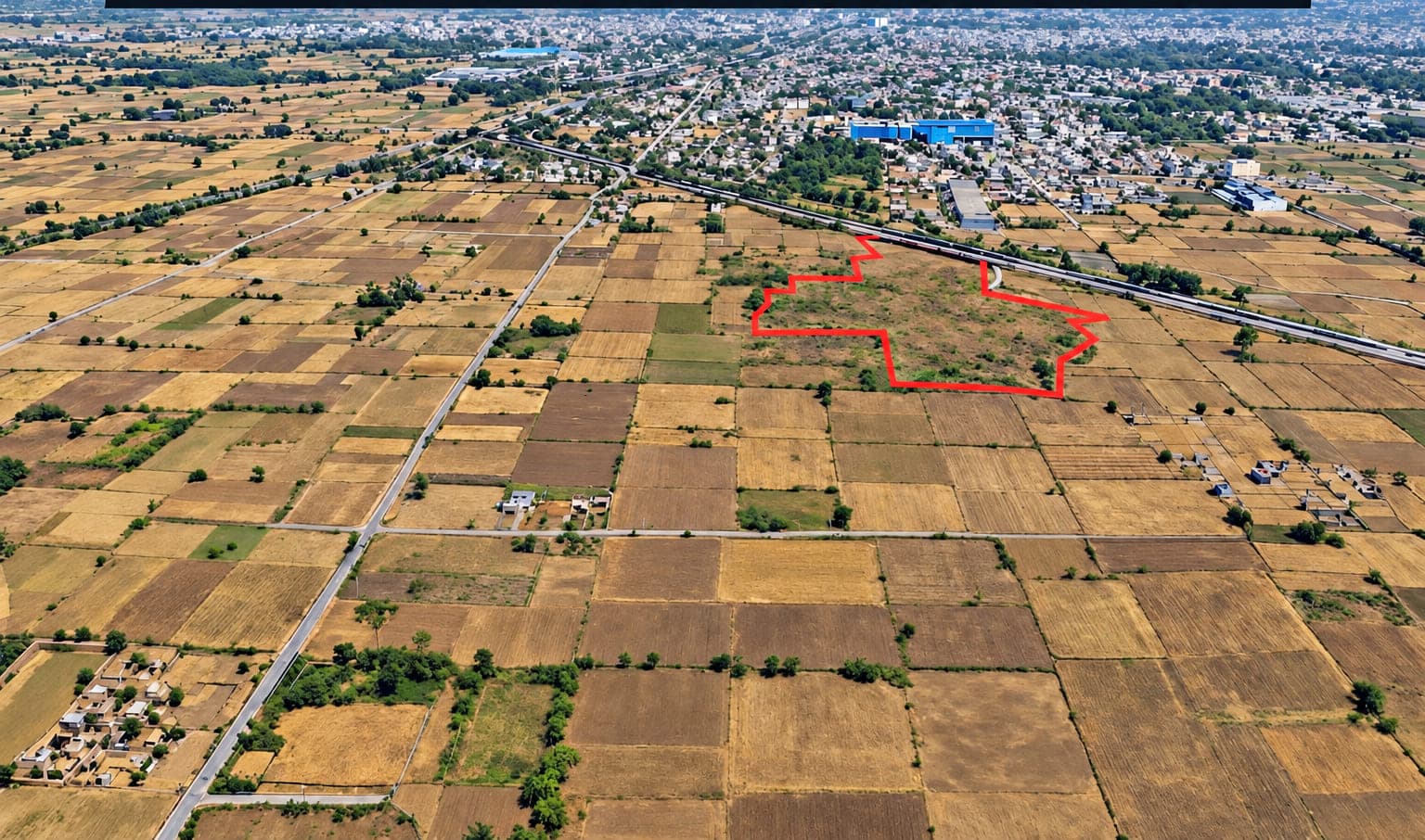 Aerial view over Pataudi with the 7.28-acre Sector 10 parcel outlined in red, bordered by farmland, a road and the built-up town beyond.